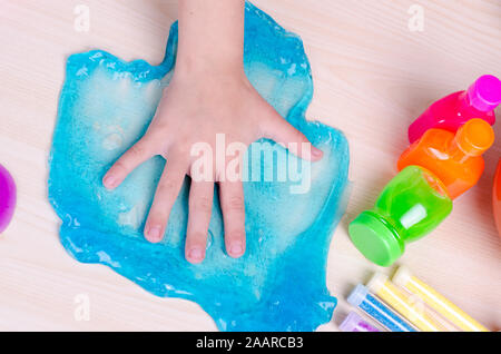 Kid's Hand zerschlagen hellen blauen Schleim auf den Tisch. Top-Down-Bild der Hand des Kindes und Schlämmen, weltweit beliebtes Spielzeug. Stockfoto