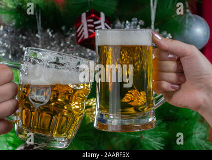 Frohes neues Jahr. Zwei Personen toasten mit zwei Pint helles Bier gegen den Weihnachtsbaum, Foto-Illustration Stockfoto