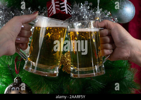 Frohes neues Jahr. Zwei Personen toasten mit zwei Pint helles Bier gegen den Weihnachtsbaum, Foto-Illustration Stockfoto