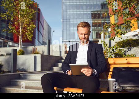 Geschäftsmann liest eine Nachricht auf Tablet auf dem Hintergrund einer Business Gebäude Stockfoto