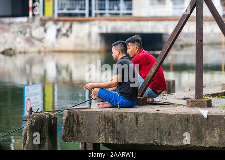 Hanoi, Vietnam - 12. Oktober 2019: Zwei asiatische Männer sitzen am Rande eines Sees in Hanoi Fisch zum Abendessen zu kochen Stockfoto