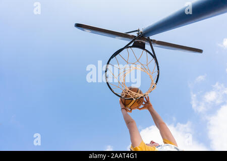 Junge einen Slam Dunk in street Basketball mit blauem Himmel und weißen Wolken Stockfoto