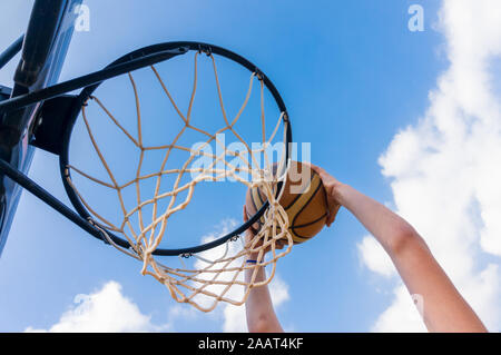 Junge einen Slam Dunk in street Basketball mit blauem Himmel und weißen Wolken Stockfoto