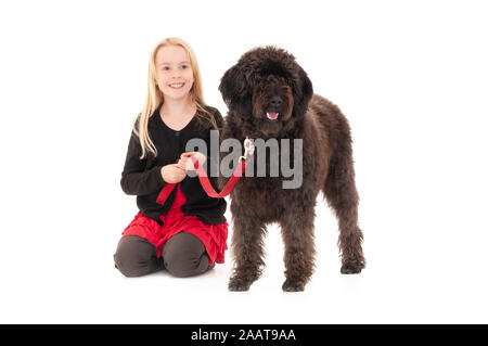 Junge blonde Mädchen, dass schwarze Labradoodle auf einem roten Leine. Auf weissem studio Hintergrund isoliert Stockfoto