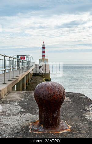 Rostige alte Anlegestelle auf einem Bootssteg mit rot-weiss gestreifte Leuchtturm im Hintergrund Stockfoto