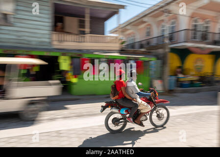 Ein Bild von einem Paar reiten ein rotes Motorrad auf der viel befahrenen Straße auf Ambergris Caye, Belize. Ein Bild mit einem panning Technik übernommen. Stockfoto