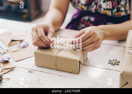 In der Nähe der Hände, die Verpackung Geschenkbox auf Holztisch mit Weihnachten Dekoration. Stockfoto