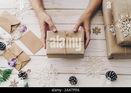 Nahaufnahme von Händen Frau vorhanden Geschenkbox auf Holztisch mit Weihnachten Dekoration. Stockfoto