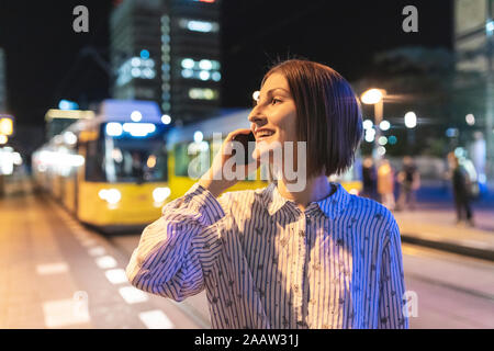 Junge Frau in die Stadt in der Nacht, am Telefon zu sprechen, Straßenbahn im Hintergrund, Berlin, Deutschland Stockfoto