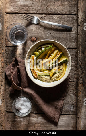 Direkt oberhalb der Schuß von Hummus mit gebratenen Zucchini in Schüssel mit Trinkwasser auf hölzernen Tisch serviert Stockfoto