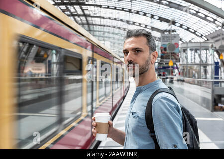 Mann mit Kaffee zum Mitnehmen am Bahnhof, während der Zug einfährt, Berlin, Deutschland Stockfoto