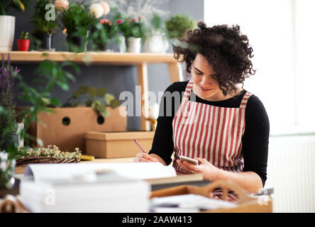 Lächelnde junge Frau mit Handy in einem kleinen Laden mit Pflanzen Stockfoto