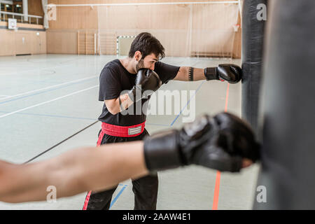 Trainer und Boxer üben an Boxsäcke in der Sporthalle Stockfoto