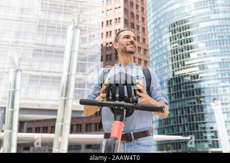 Lächelnder Mann mit e-Scooter auf Platz der Stadt, Berlin, Deutschland Stockfoto