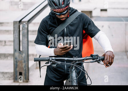 Stilvolle Junger Mann mit Fahrrad, Smartphone und Messenger Bag in der Stadt Stockfoto