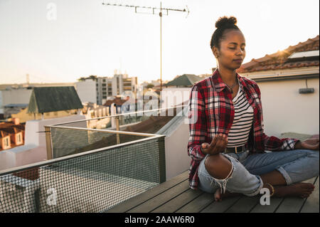 Junge Frau mit Yoga auf der Dachterrasse bei Sonnenuntergang Stockfoto