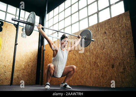 Junge brünette Frau tun Overhead hocke Übung im Fitnessstudio Stockfoto