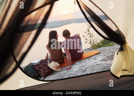 Foto von glücklichen Paare im Zelt sitzen mit Blick auf den See während der Wanderung. Reisen Abenteuer Urlaub Konzept Stockfoto