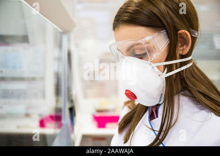 Junge Frau mit Schutzmaske und Schutzbrille, während in einem Labor arbeiten Stockfoto