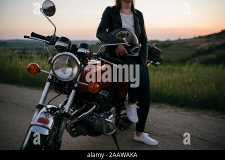 Erntegut schoss der jungen Frau mit Vintage Motorrad auf der Landstraße bei Sonnenuntergang, Toskana, Italien Stockfoto