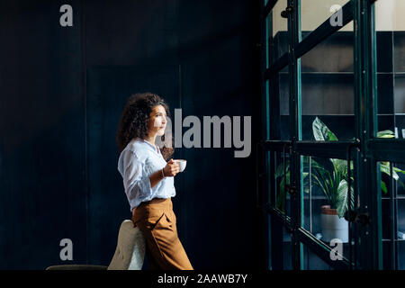 Junge Geschäftsfrau Blick aus Fenster in loft Büro Stockfoto