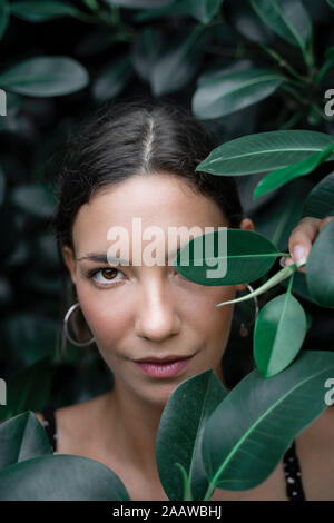 Porträt der jungen Frau versteckt sich hinter grünen Blätter Stockfoto