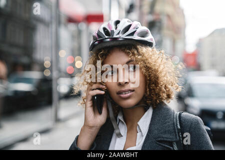 Portrait von Frau mit Fahrrad Helm, am Telefon zu sprechen in der Stadt, Berlin, Deutschland Stockfoto