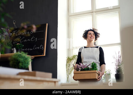 Glückliche junge Frau mit Blumen in einem Karton in einem kleinen Laden Stockfoto