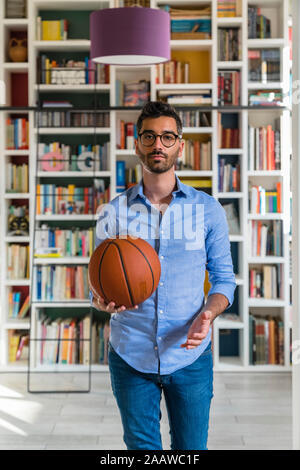 Porträt eines jungen Mannes mit Basketball stand vor der Bücherregale zu Hause Stockfoto