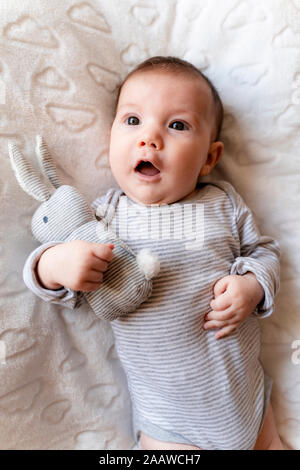 Baby Mädchen liegt auf einer weißen Decke mit Wolken und ein Kaninchen Spielzeug Stockfoto