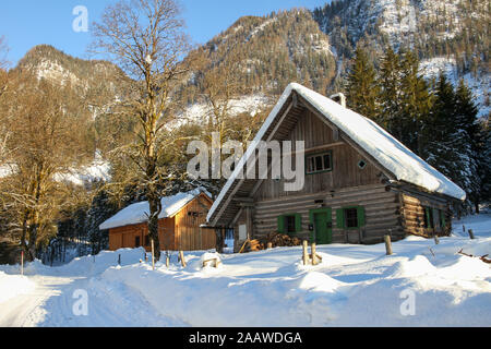Nette kleine alpine Chalet mit einem Stapel von Holz vor im Schnee bedeckt. Typische Szene für den Europäischen Alpen mit Bergen und Bäumen im Hintergrund Stockfoto