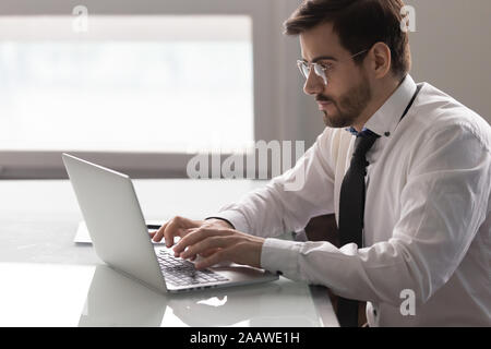 Geballte männliche Angestellte arbeitet am Laptop Stockfoto