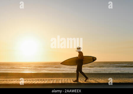 Surfer gehen mit dem Surfbrett in den Sonnenuntergang am Strand Stockfoto