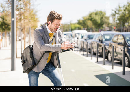 Junge Unternehmer mit e-Scooter mit Handy in der Stadt Stockfoto