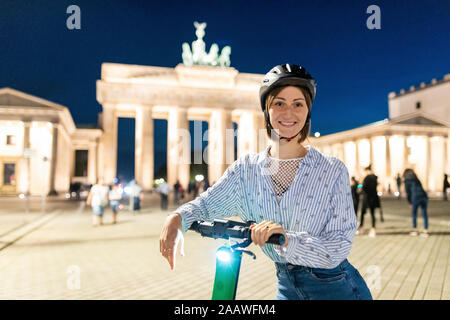 Junge Frau mit einem elektrischen scooter am Brandenburger Tor bei Nacht, Berlin, Deutschland Stockfoto