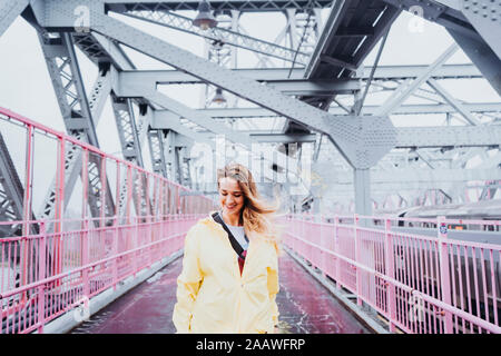 Eine Frau tragen gelbe Regenmantel, wandern auf einer Brücke und nach unten schaut, New York, USA Stockfoto
