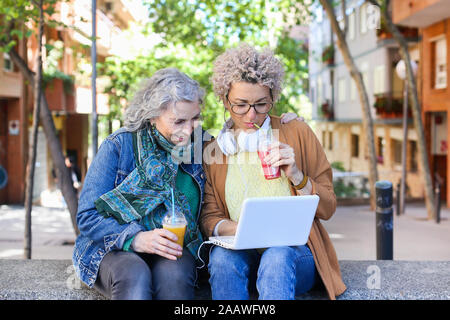 Ältere Mutter mit ihrer erwachsenen Tochter mit Laptop und trinken Säfte in der Stadt Stockfoto