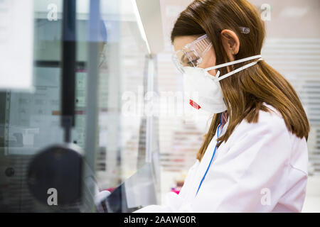 Junge Frau mit Schutzmaske und Schutzbrille, während in einem Labor arbeiten Stockfoto