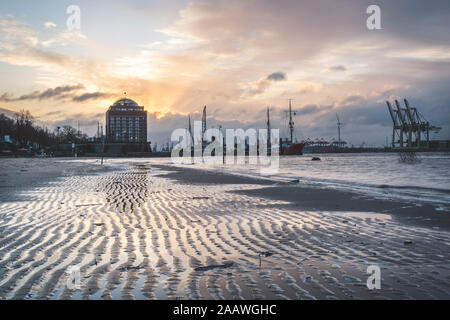 Schiffe und Kräne am Hafen gegen bewölkter Himmel bei Sonnenuntergang, Hamburg, Deutschland Stockfoto