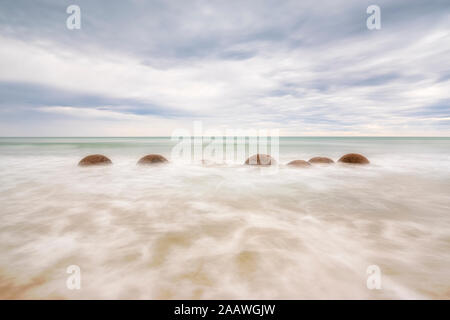 Moeraki Boulders im Meer am Strand gegen Koekohe bewölkter Himmel, Neuseeland Stockfoto