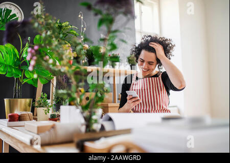 Glückliche junge Frau mit Handy in einem kleinen Laden mit Pflanzen Stockfoto