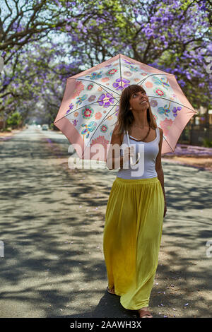 Frau wandern mit ihrem Schirm auf einer Straße, Jacaranda Bäume in Blüte, Pretoria, Südafrika Stockfoto