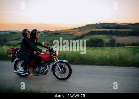 Junges Paar reiten vintage Motorrad auf der Landstraße bei Sonnenuntergang, Toskana, Italien Stockfoto