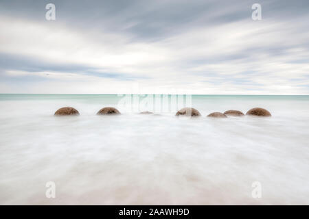 Moeraki Boulders im Meer am Strand gegen Koekohe bewölkter Himmel bei Sonnenuntergang, Neuseeland Stockfoto