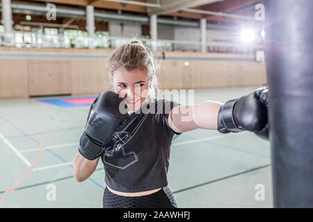 Lächelnd weibliche Boxer üben an Boxsack in der Sporthalle Stockfoto