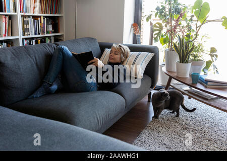 Reife Frau entspannen auf der Couch zu Hause ein Buch lesen Stockfoto