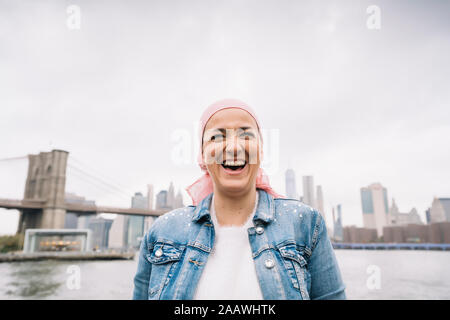 Portrait von lachende Frau mit Krebs bandana an der Brooklyn Bridge in New York, USA Stockfoto