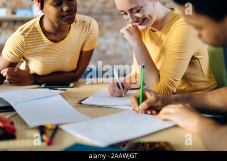 Junge Menschen sitzen zusammen am Tisch und Notizen Stockfoto