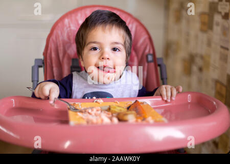 Portrait von kleinen Jungen sitzen auf hohen Stuhl Gemüse essen Stockfoto