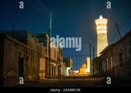 Straße mit Wohnhäusern gegen große Minarett der Kalon in Buchara, Usbekistan. Es ist ein Minarett der Po-i-Kalyan Moschee Komplex in Buxo Stockfoto